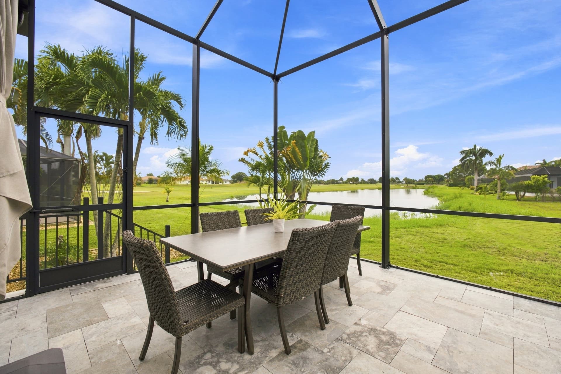 Screened lanai with outdoor dining table overlooking a lake and golf course